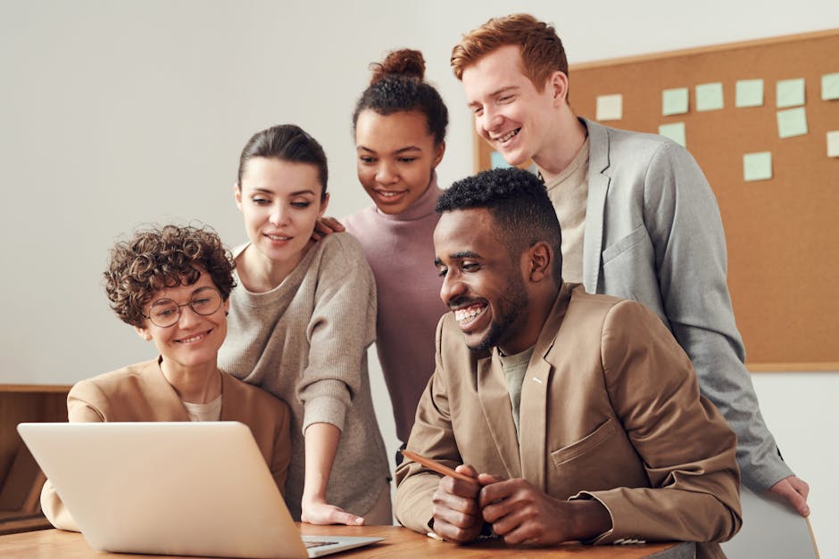 A group of diverse young professionals happily collaborating around a laptop indoors