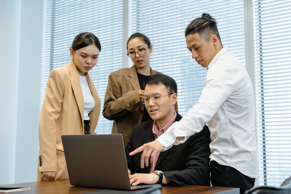 A group of professionals engage in teamwork around a laptop in a modern office setting